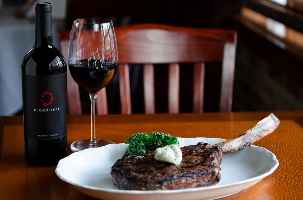 Wagyu Tomahawk steak with a bottle of Bloodlines Cabernet Sauvignon and a glass of red wine